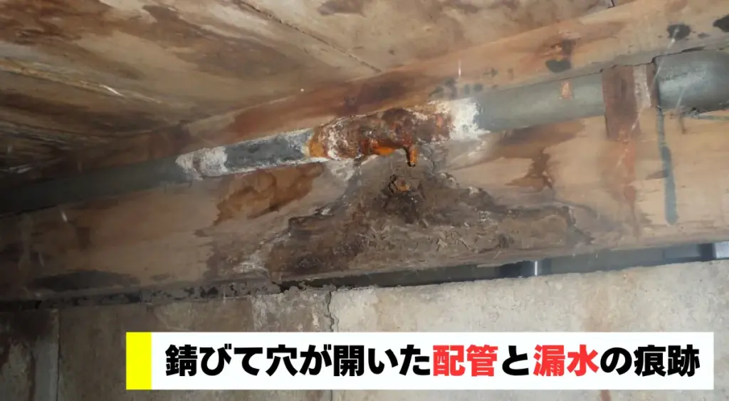 錆びて穴が開いた配管と漏水の痕跡